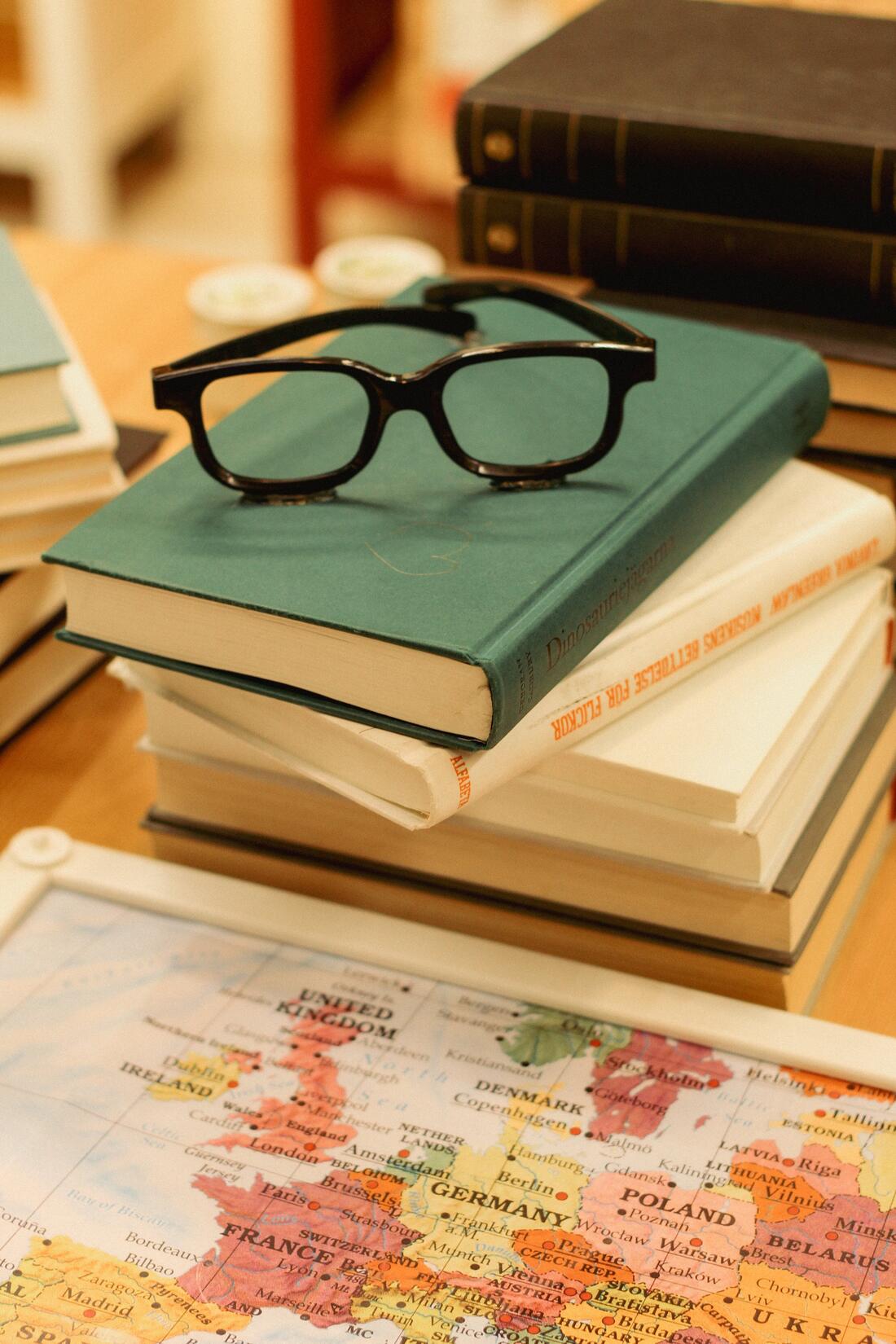 Stabel med bøker med briller på toppen. I forgrunnen ser vi deler av et verdenskart.