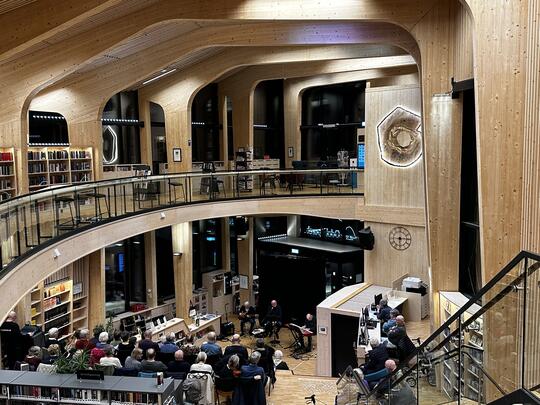 Oversiktsbilde under konsert i biblioteket, publikum i trappa og artister nede foran resepsjonen